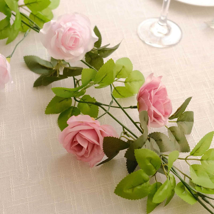 Artificial pink rose garland with green leaves on a table setting.