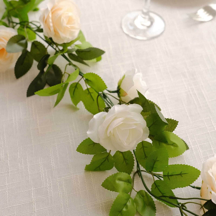 Artificial white rose garland with green leaves on a table setting.