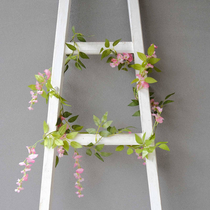 White ladder adorned with pink flowers and green leaves against a gray background.