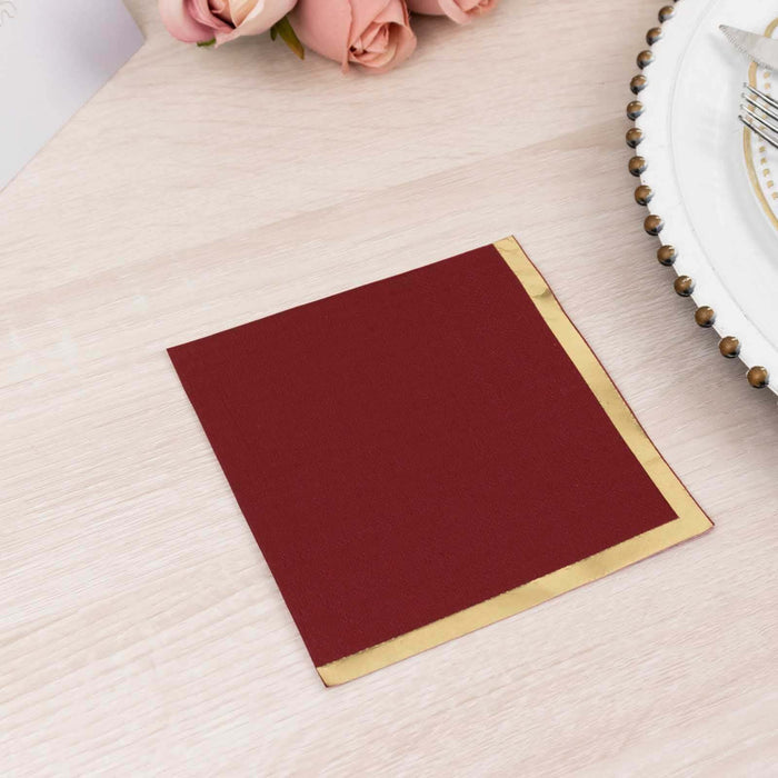Burgundy napkin with gold trim on a wooden table setting.