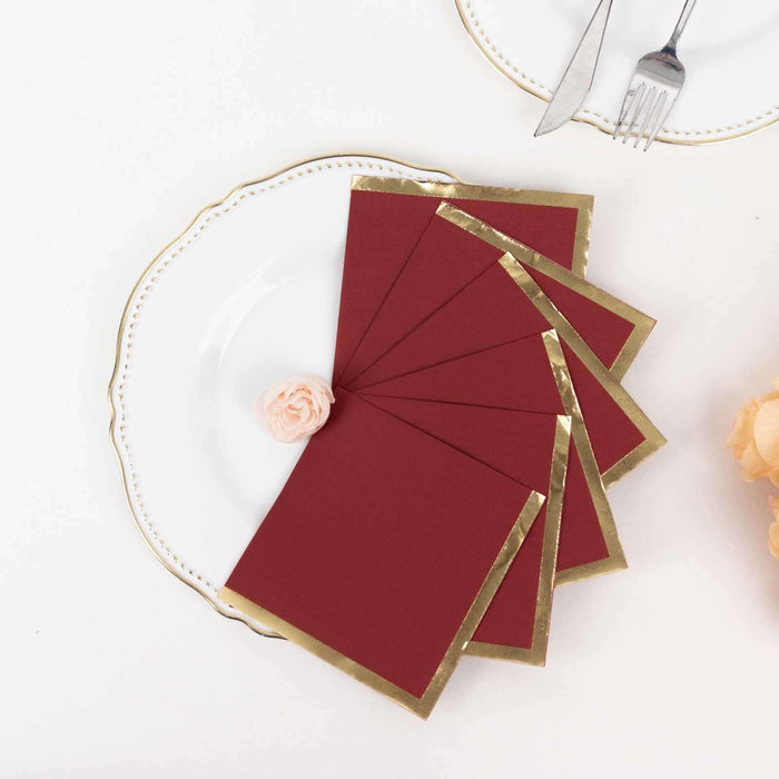 Elegant burgundy envelopes with gold trim displayed on a white plate.
