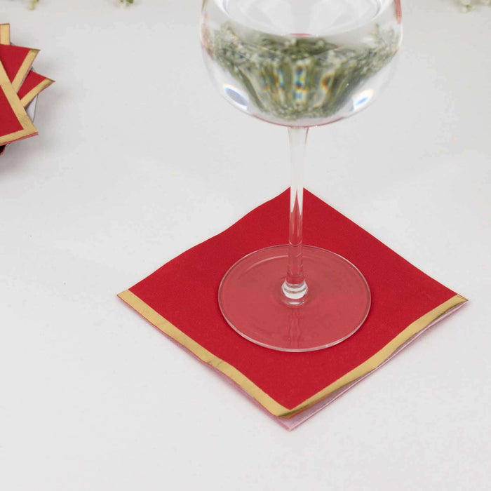 Red napkin with gold trim under a glass on a table.