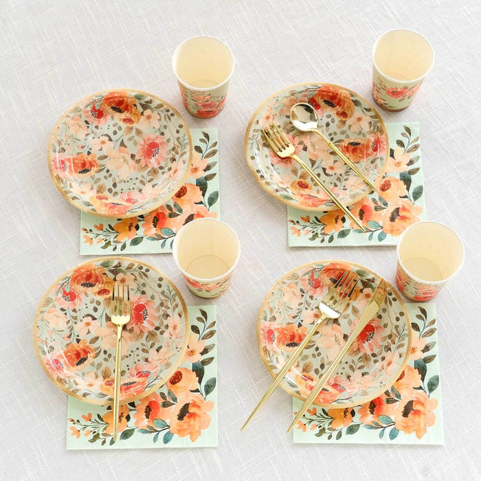 Floral dinnerware set with plates, cups, and utensils on a textured tablecloth.
