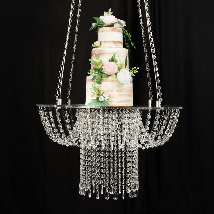 Elegant three-tier wedding cake with floral accents hanging from a chandelier.