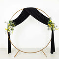 Gold circular wedding arch with black drapery and floral accents