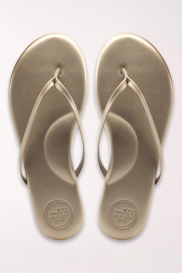 Pair of champagne gold flip-flops on a white background