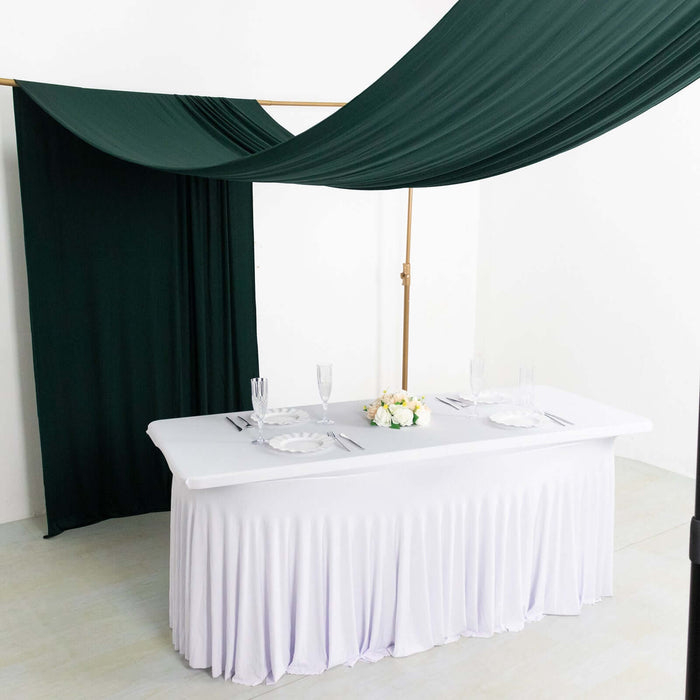 Elegant dining table setup with white tablecloth and green drapery.