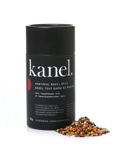 A black shaker bottle labeled 'kanel. Montreal Bagel Spice' with a pile of multiseed seasoning mix in front of it.