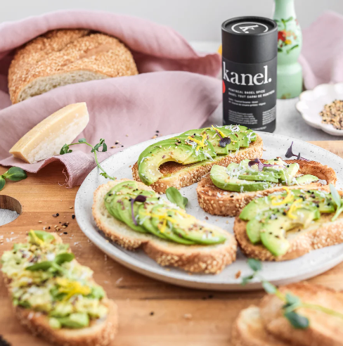 Avocado toast on a white plate with a black cannister of Kanel Montreal Bagel Spice Seasoning.
