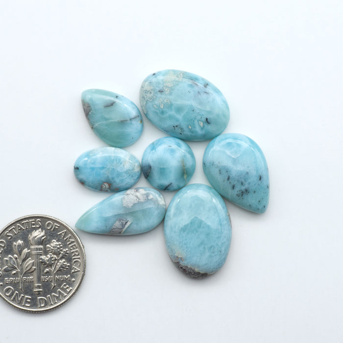 Larimar stone cabochons, cut and polished, blue and white gemstones on a white background, with a US dime for scale