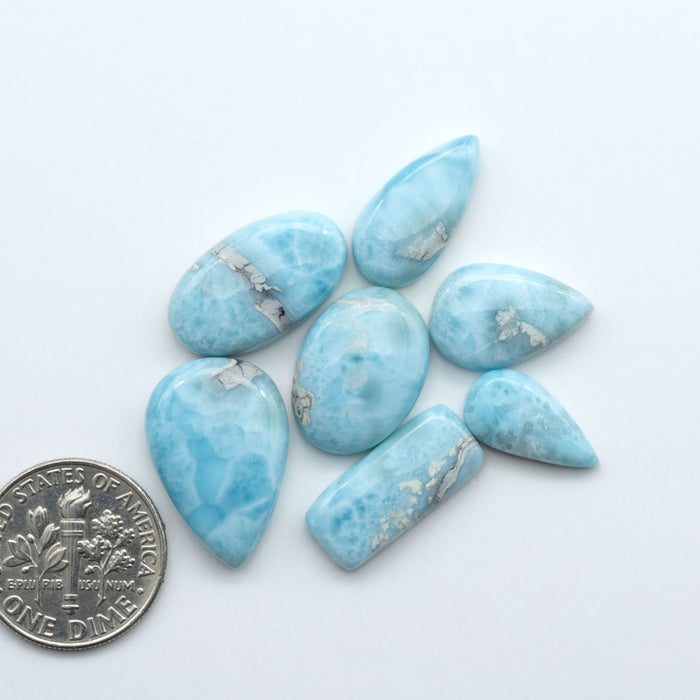 Larimar stone cabochons, cut and polished, blue and white gemstones on a white background, with a US dime for scale