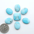 Pressed Turquoise nugget cabochons, composite material with a blue color and dark matrix on a white background, with a US dime for scale.