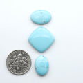 Pressed Turquoise nugget cabochons, composite material with a blue color and dark matrix on a white background, with a US dime for scale.