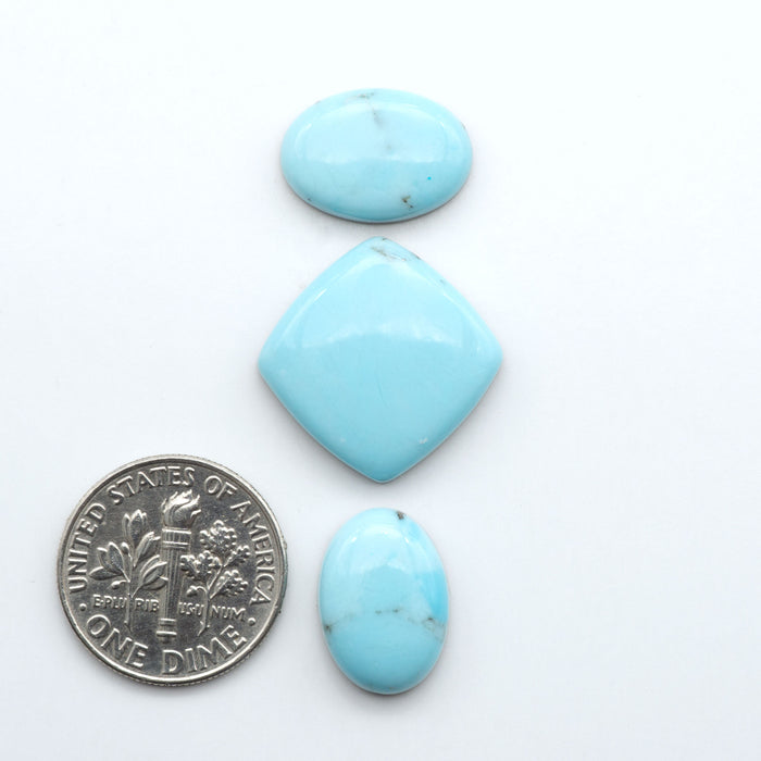 Pressed Turquoise nugget cabochons, composite material with a blue color and dark matrix on a white background, with a US dime for scale.