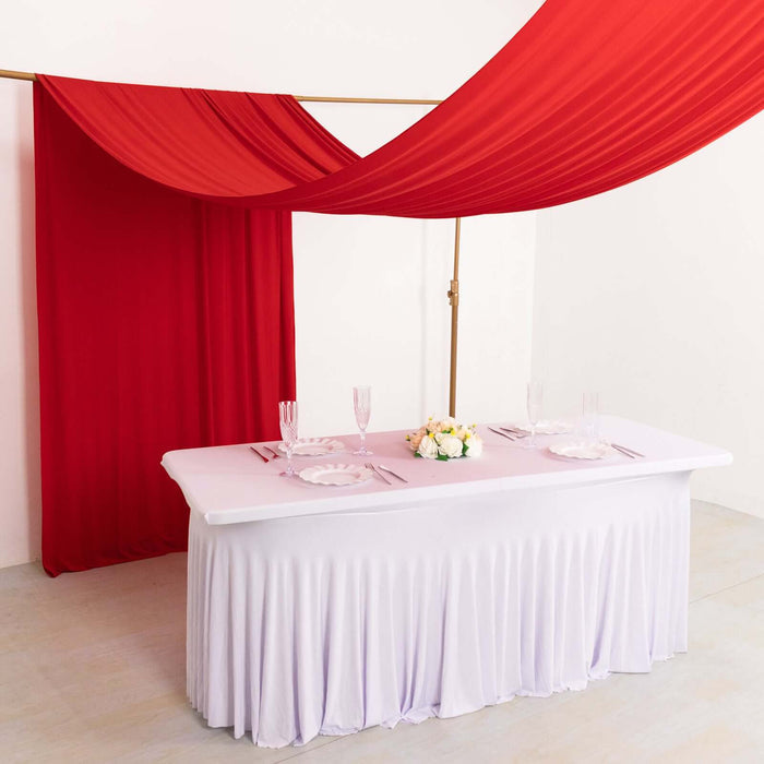 Elegant table setup with white tablecloth, glassware, and red drapery.