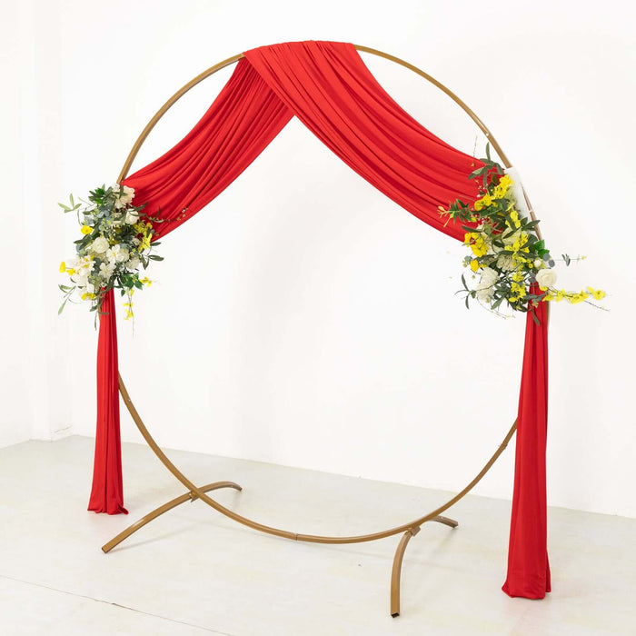 Red draped wedding arch with floral arrangements on a white backdrop.