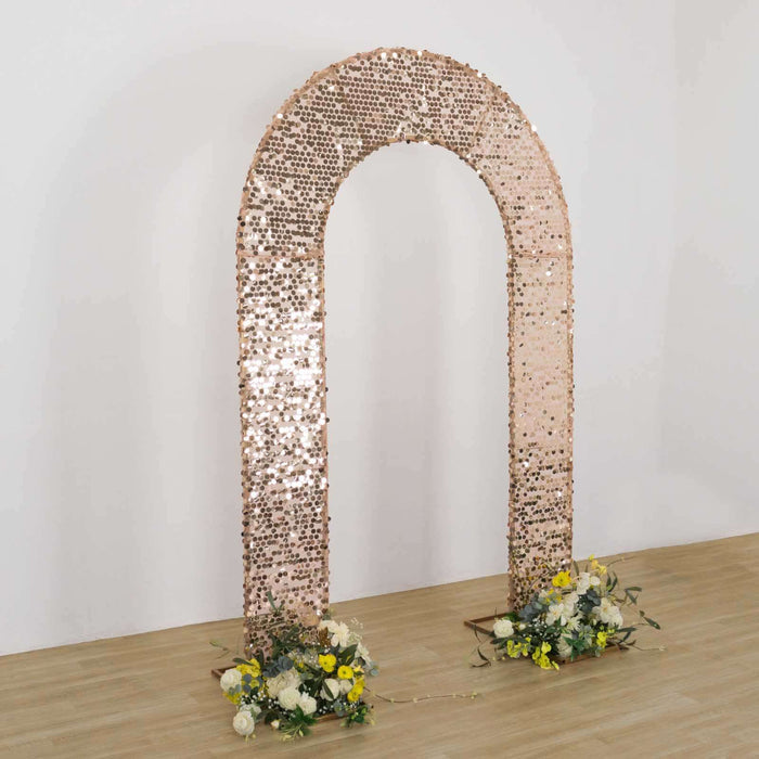 Rose gold sequin arch with floral arrangements on a wooden floor.