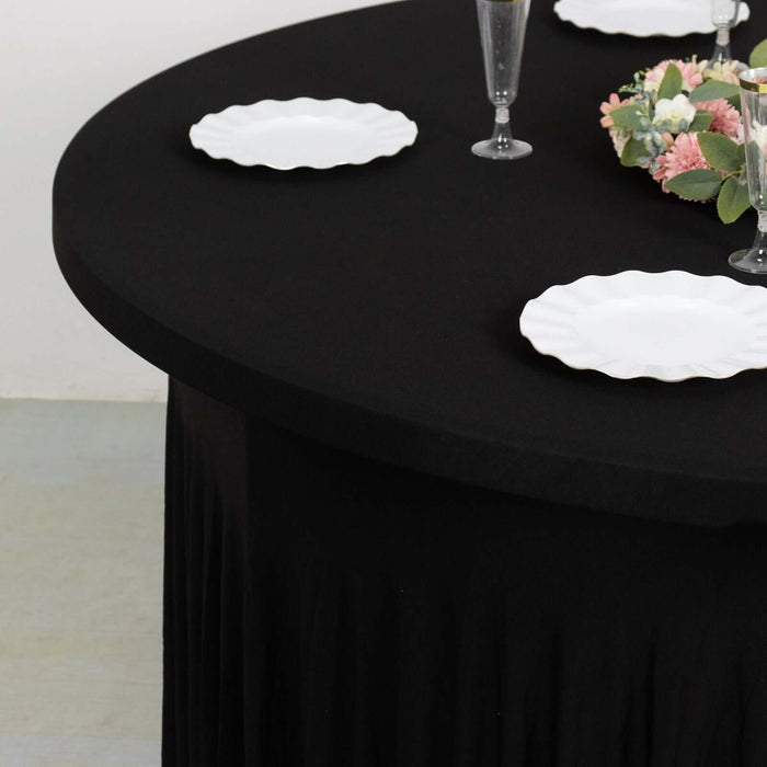 Black tablecloth draped on round table with white plates and floral centerpiece.