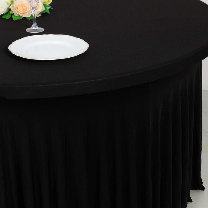 Black tablecloth draping over a round table with a white plate and floral centerpiece.