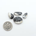 Four black and white marbled stones with a U.S. dime for scale on a white background. White Buffalo Stone Cabochons
